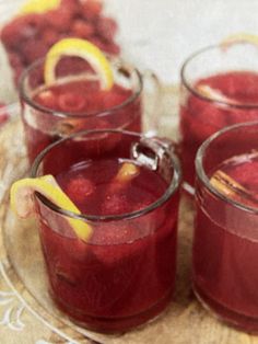 three glasses filled with red liquid on top of a glass plate next to sliced fruit