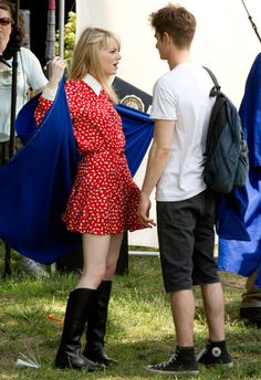 a woman in a red dress and black boots holding a blue jacket while standing next to a man