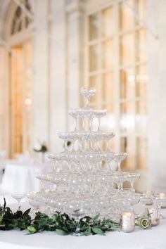 a white table topped with a tall glass cake stand filled with wine glasses and greenery