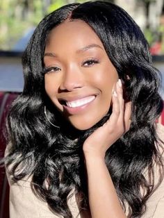 a woman with long black hair smiling and holding her hand up to her face,