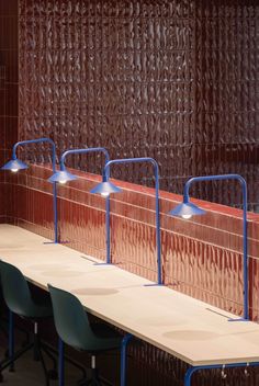 three long tables with blue chairs next to each other in front of a brown wall