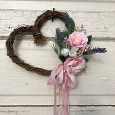 a heart shaped wreath with pink flowers and greenery hanging on the side of a door