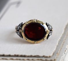 "A dramatic vintage ring designed in the Georgian style, of European origins. Crafted in 18k yellow gold and silver, featuring a deep red foiled garnet set in a gold cut-down collet cup, accented by bright single-cut diamonds set in dainty sterling tulips on the shoulders. Late 18th century details are faithfully copied from the sunray design engraved on the back of the garnet's seat to the ornate Rococo-style band. Measuring approximately 1/2\" north to south across the face with a rise of 5.6 Elegant Red Intaglio Signet Ring, Antique Red Gemstone Signet Ring, Antique Garnet Rings As Gift, Ornate Garnet Round Rings, Georgian Rings Antique, Vintage Garnet Rings With Polished Finish, Luxury Antique Garnet Rings, Ornate Red Garnet Jewelry, Garnet And Diamond Ring