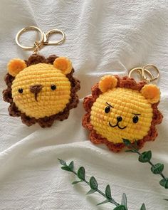 two keychains made to look like animals are sitting on a white sheet with green leaves