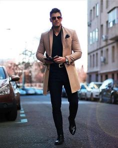 a man walking down the street wearing a tan coat and black shirt with his hands in his pockets