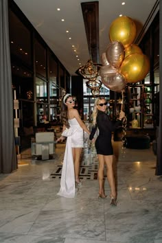 two women dressed in black and white posing for the camera with gold balloons behind them