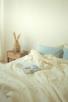 an unmade bed with white sheets, blue pillows and a basket on the end table