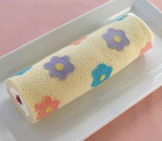 a roll of toilet paper with flowers on it sitting in a white tray next to a pink tablecloth