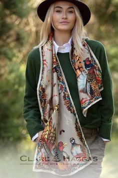 Woman wearing a green sweater and wide-brimmed hat, modeling a colorful bird-patterned scarf, outdoors.