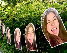 a group of people hanging from a line with pictures of them on clothes pins in front of some bushes