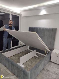 a man standing next to a bed with a mattress on it's back end