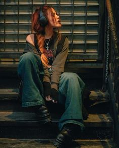 a woman with headphones sitting on the steps in front of a metal door and stairs