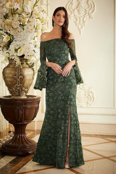 a woman in a green dress standing next to a vase with white flowers on it