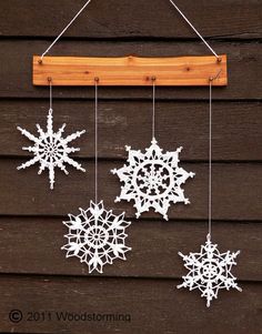 three snowflakes are hanging from a wooden hanger on the side of a building