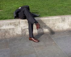 a man in a suit and tie laying on the ground next to a stone wall