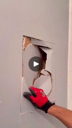 a person in red gloves is working on a wall with a hole cut into it