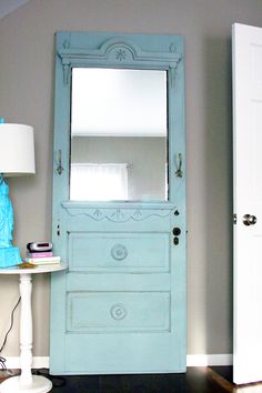 a room with a blue door, mirror and lamp on the floor next to it