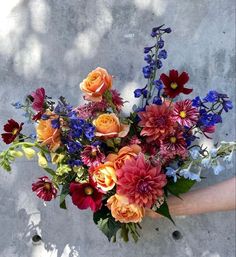 a bouquet of flowers in someone's hand on a concrete surface with sunlight coming through the leaves