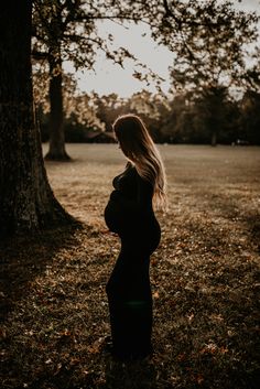 a pregnant woman standing in front of a tree