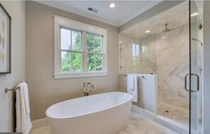 a large white bathtub sitting under a window in a bathroom next to a walk in shower