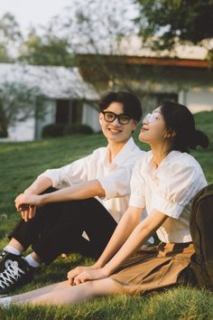 two people sitting on the grass in front of a house