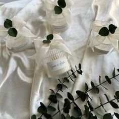 three small bottles with white flowers in them on a table cloth next to some green leaves