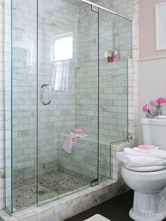 a white toilet sitting next to a walk in shower under a bathroom mirror with pink flowers on it