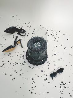 a birthday cake with black stars on the table next to high heel shoes and sunglasses