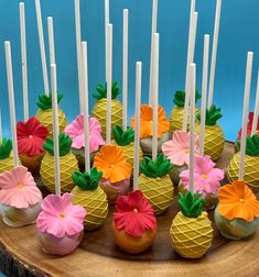 cupcakes decorated with flowers and pineapples on a wooden platter