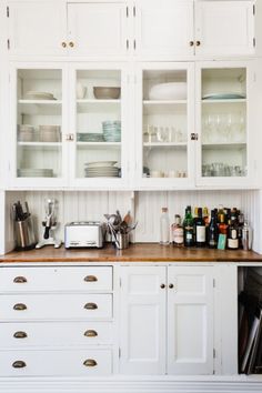 a kitchen with white cabinets and wooden counter tops, along with dishes on the shelves