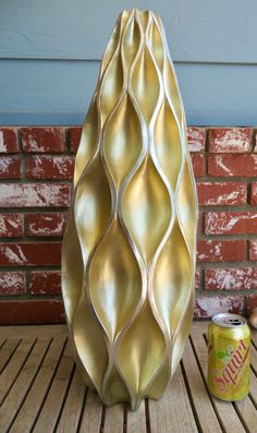 a gold vase sitting on top of a wooden table next to a can of soda