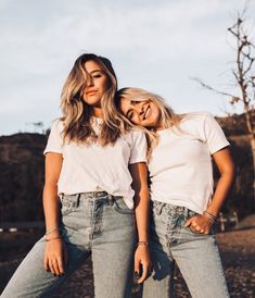 two beautiful young women standing next to each other in front of a field with trees