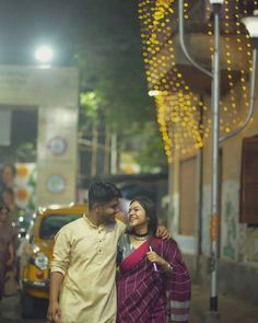 a man and woman standing next to each other in front of a building with lights on it