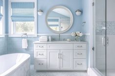 a bathroom with blue walls and white fixtures, including a large round mirror above the sink