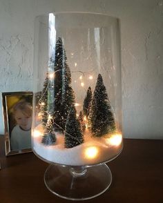 a glass vase filled with snow and lit up trees on top of a wooden table