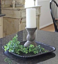 a candle sits on top of a black tray with green plants in it and a white candle