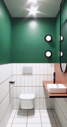 a white toilet sitting next to a bathroom sink in a green and white tiled room