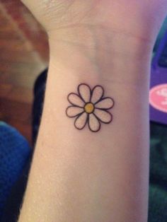 a small tattoo on the wrist of a woman with a flower in it's center