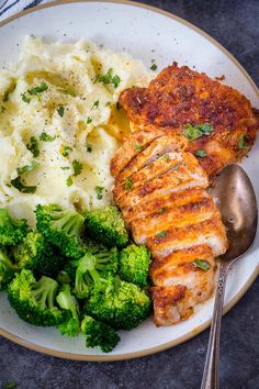 a white plate topped with meat, mashed potatoes and broccoli next to a fork