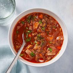 a bowl of soup with meat and vegetables in it next to a glass of water