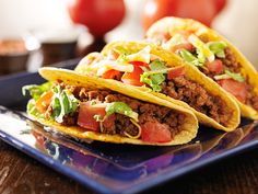 three tacos on a plate with lettuce and tomatoes in the back ground