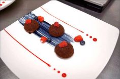 three chocolate desserts with raspberries and blueberries are on a white plate