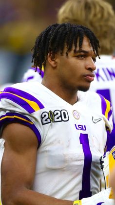 a close up of a football player with dreadlocks standing on the sidelines