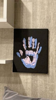 a black and blue handprint on a wall next to a white shelf with a gray pillow