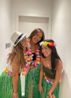 three women in grass skirts and flower leis posing for the camera with their arms around each other