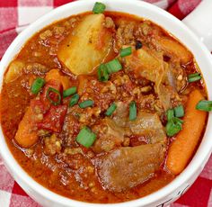 a white bowl filled with stew on top of a red and white checkered table cloth