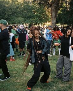 a woman with dreadlocks dancing in front of a group of people on the grass