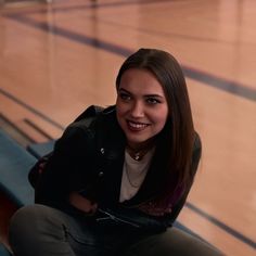 a woman sitting on the floor in front of a basketball court smiling at the camera