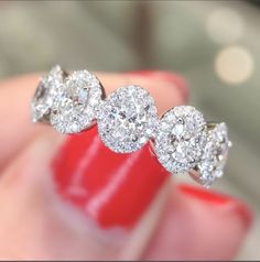 a woman's hand holding an engagement ring with three diamonds on it and red nail polish