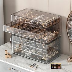 three clear drawers with gold rings and other jewelry on top of a marble countertop